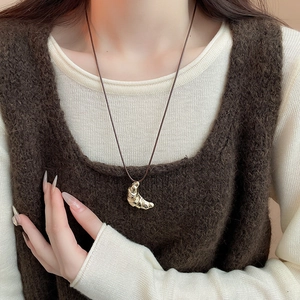 Close-up of golden croissant pendant on a dark brown leather cord necklace