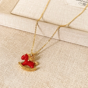 Detail of red rocking horse pendant with golden chain on beige fabric texture