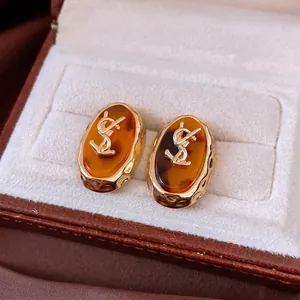 Vintage gold oval stud earrings with amber resin texture and iconic metallic logo inlay