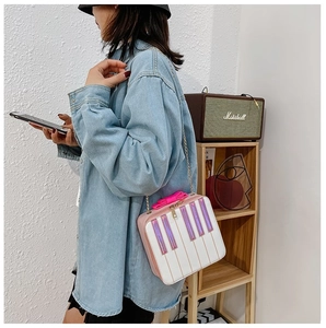 Pink piano-shaped crossbody bag with bow detail worn by model in a minimalist room