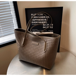 Detail of woven texture and brand tag on earth-tone tote bag with slim shoulder straps