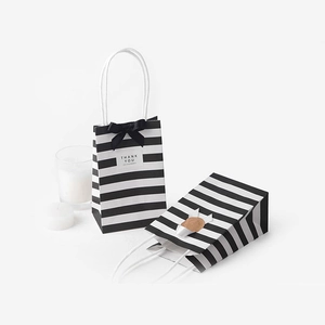 Vertical striped white kraft gift bags with black bow and Thank You tag on white background