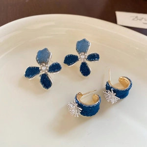 Detailed view of floral denim earrings with gold rings and charms on a ceramic tray