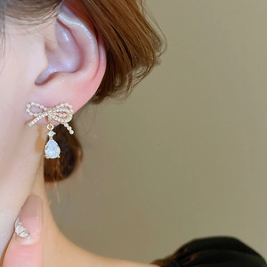 Close-up of gold bow earrings with pearls and a teardrop zircon on a model's ear