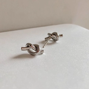 Detailed view of silver S925 sterling silver knotted stud earrings on white texture