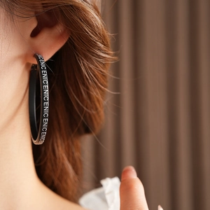 Gros plan d'une boucle d'oreille créole noire en cuir avec imprimé de lettres blanches