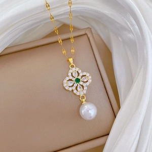 Detail of gold four-leaf clover pendant with green gemstone and hanging pearl on silk