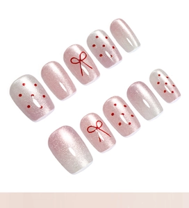 Detail of pink cat-eye press-on nails with red polka dots and bow tie nail art designs