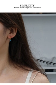 Close-up of golden zircon earrings with blue crystal pendant worn on female model's ear