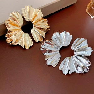 Macro view of pleated leaf-shaped earrings in gold and silver finish on leather