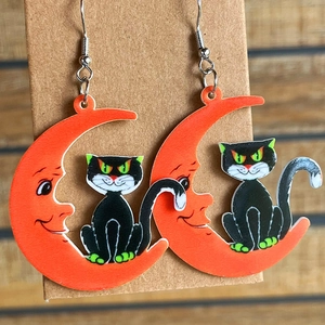 Detail of Halloween acrylic earrings featuring a black cat sitting on an orange moon charm
