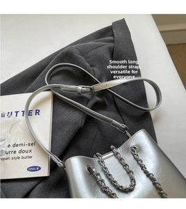 Detailed view of silver bucket bag with metal chain handle on a grey blazer