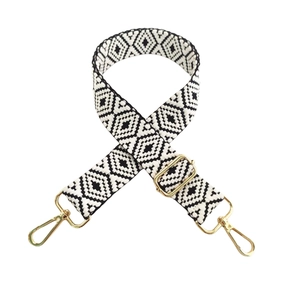 Detail of adjustable black and white geometric embroidery bag strap with gold metal buckles