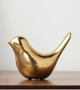 Close-up of a glossy gold ceramic bird figurine on a dark wooden table surface