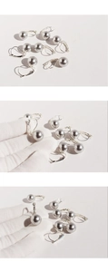 Macro shot of silver U-shaped hoop earrings with grey pearls held by a gloved hand