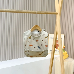 Detail of waterproof baby bib with dinosaur patterns and a built-in food catcher pocket
