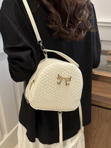 Zaino bianco intrecciato con fiocco dorato indossato da una modella in interno elegante