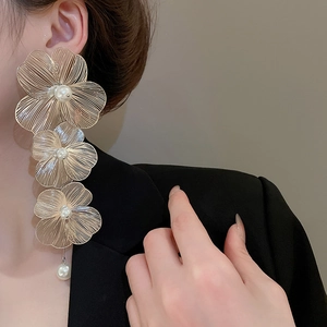Dettaglio di grandi orecchini a fiore dorati con perle indossati da una modella in nero