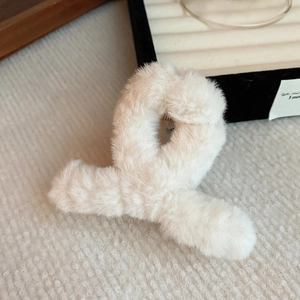 Close-up of the plush white faux fur cross hair claw clip on a textured beige surface