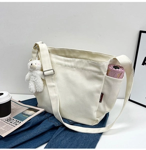White canvas messenger bag with a bear pendant and side pocket holding a pink umbrella