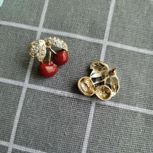 Détail de boucles d'oreilles cerises rouges avec feuilles dorées et strass sur tissu