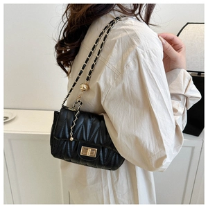 On-shoulder view of black quilted crossbody bag with gold chain and ball charm
