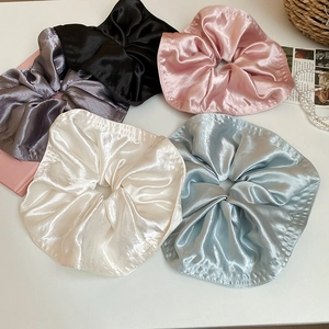 Flat lay of five large satin scrunchies in assorted soft colors with pearls on white background