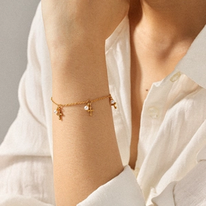 Golden stainless steel chain bracelet with cross charms and white pearls on woman's wrist