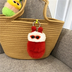 Detail van schattige rood-witte pluche rups hanger met zonnebril aan een geweven tas