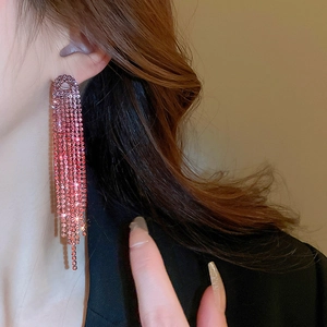 Close-up of pink rhinestone long tassel earrings worn by a model in warm light