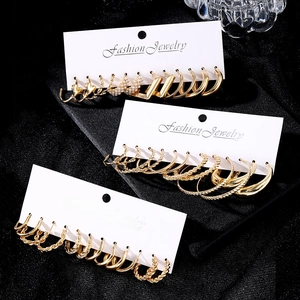 9-piece gold twist chain and pearl hoop earring set on black textured background