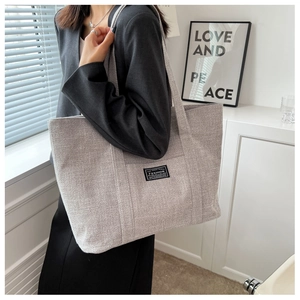 Detail showing high-capacity grey canvas tote bag texture with fashion label stitching
