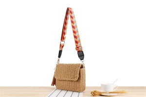 Detail of hand-woven straw crossbody bag with colorful geometric strap and leather tassel