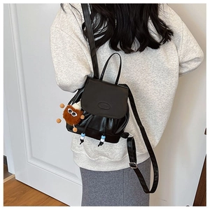 Detail view of mini black PU leather backpack with a brown plush charm on a model