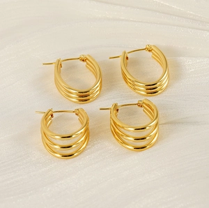 Detailed view of two pairs of gold triple-layered hoop earrings on white textured fabric
