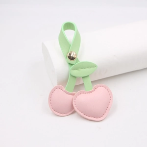 Pastel pink leather cherry bag charm with green leaves on a minimalist white stand
