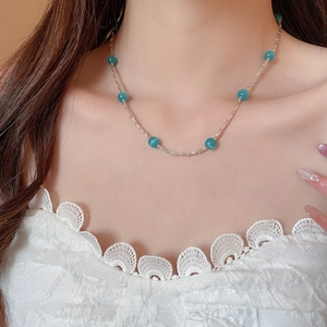 Dettaglio della collana d'argento con perline blu-verdi indossata da modella in pizzo