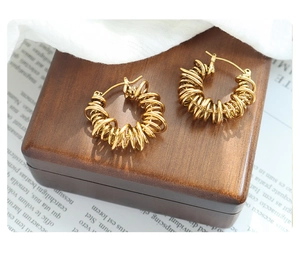 Detailed view of gold wrapped geometric U-shaped hoop earrings on a wooden box