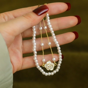 Detailed close-up of double-layer camellia pearl bracelet with gold plating on green background