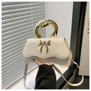 Detail of cream white handbag featuring irregular gold metal handle and bow clasp