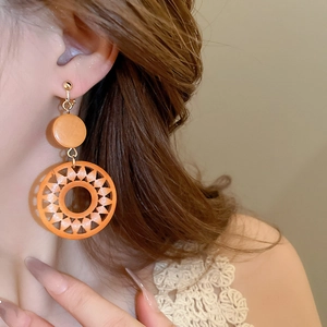Close-up of model wearing geometric sunburst wood clip-on earring in warm orange brown