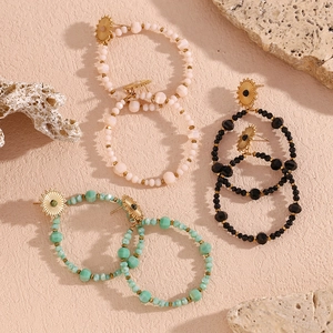 Detailed top view of beaded hoop earrings in pink, black and green with gold sunray studs