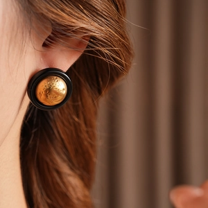Close-up of a vintage black and gold textured round earring worn on a female model
