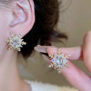 Close-up of golden snowflake stud earrings with sparkling cubic zirconia on a model