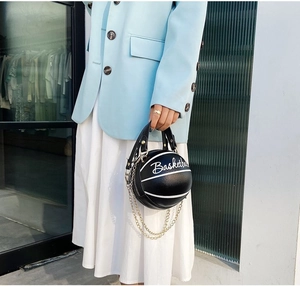 Fashionable black basketball shaped crossbody bag with gold chain shown on a model