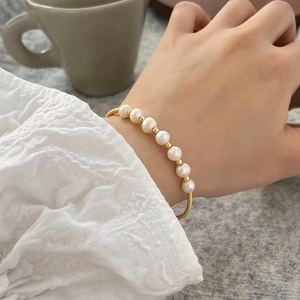 Detailed view of model wearing natural pearl bracelet with gold beads and metal band
