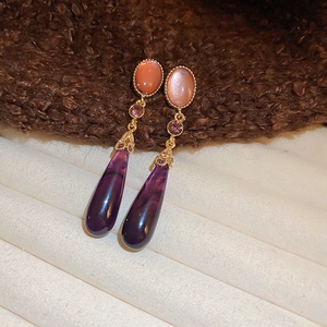 Macro detail of gothic vintage earrings with purple resin teardrop and gold accents
