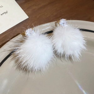Détail de boucles d'oreilles pompon blanc avec zircon cubique rond et placage d'or luxueux