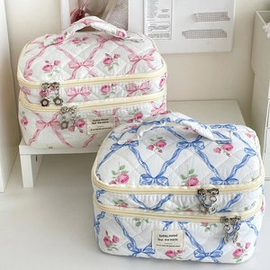 Détail de trousse de maquillage matelassée fleurie avec double fermeture et ruban