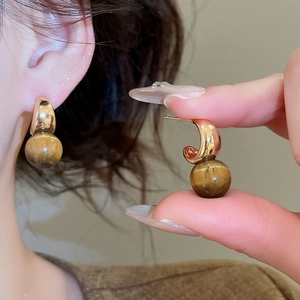 Macro detail of 18k gold plated hoop earrings featuring a natural tiger eye stone bead
